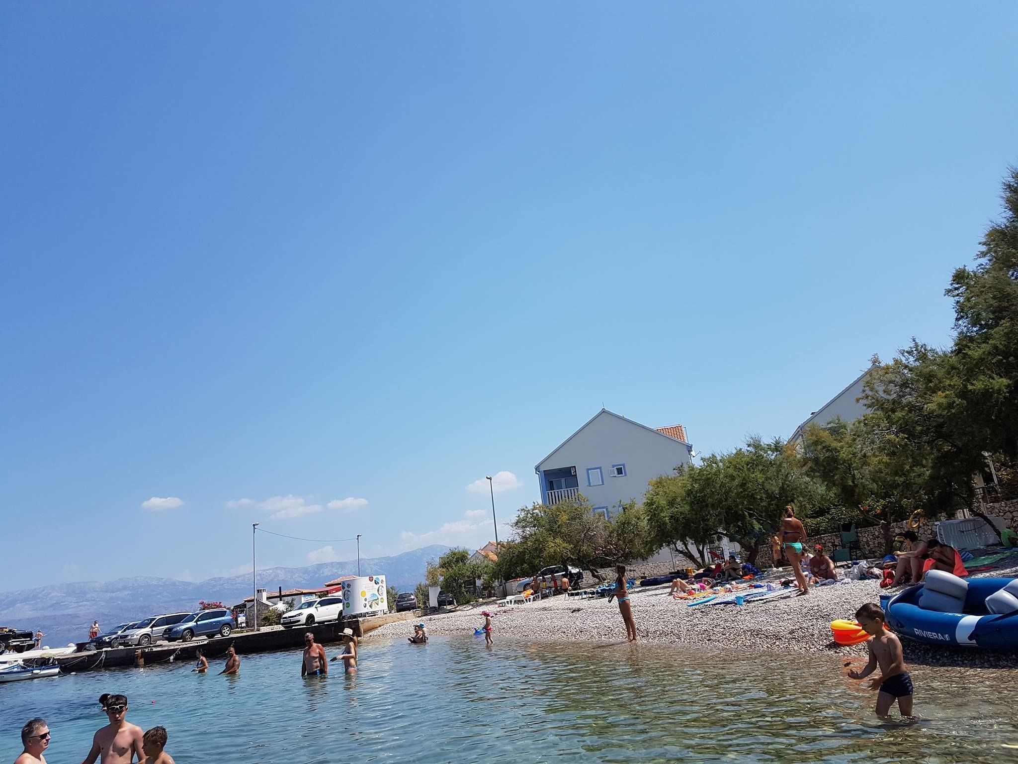 En strand med klart vand, folk der svømmer, og både i havnen.