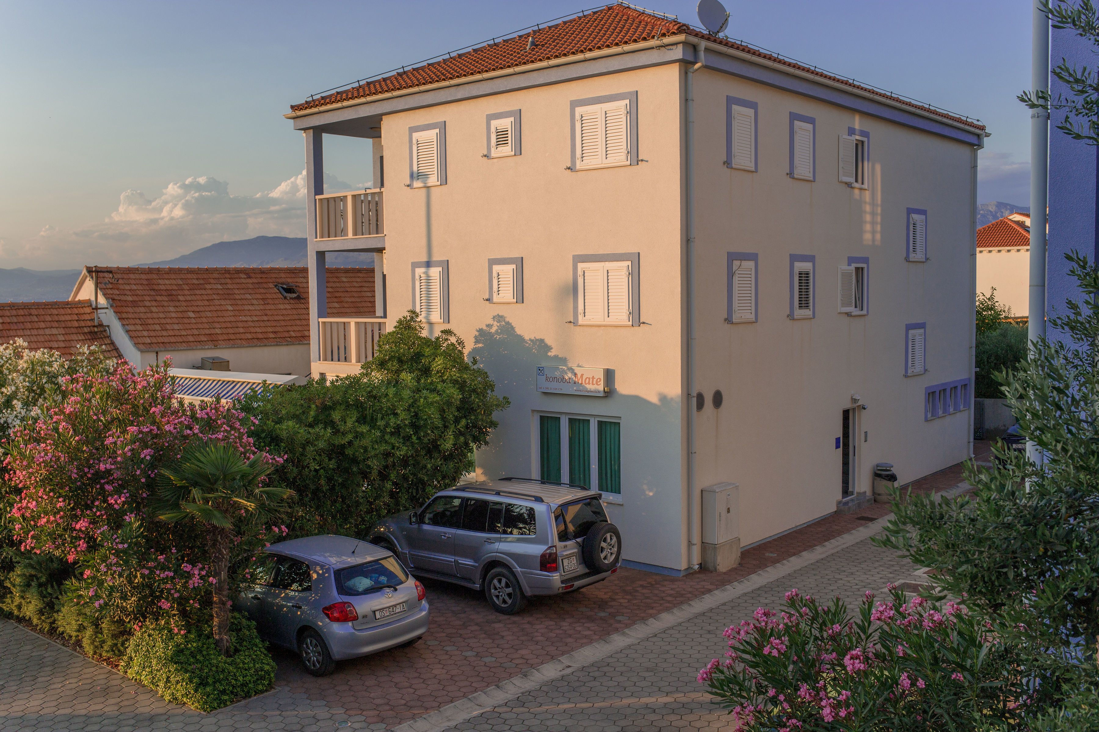 A two-story building with a balcony, a car parked in front, and a sign that reads "Hotel Mate".