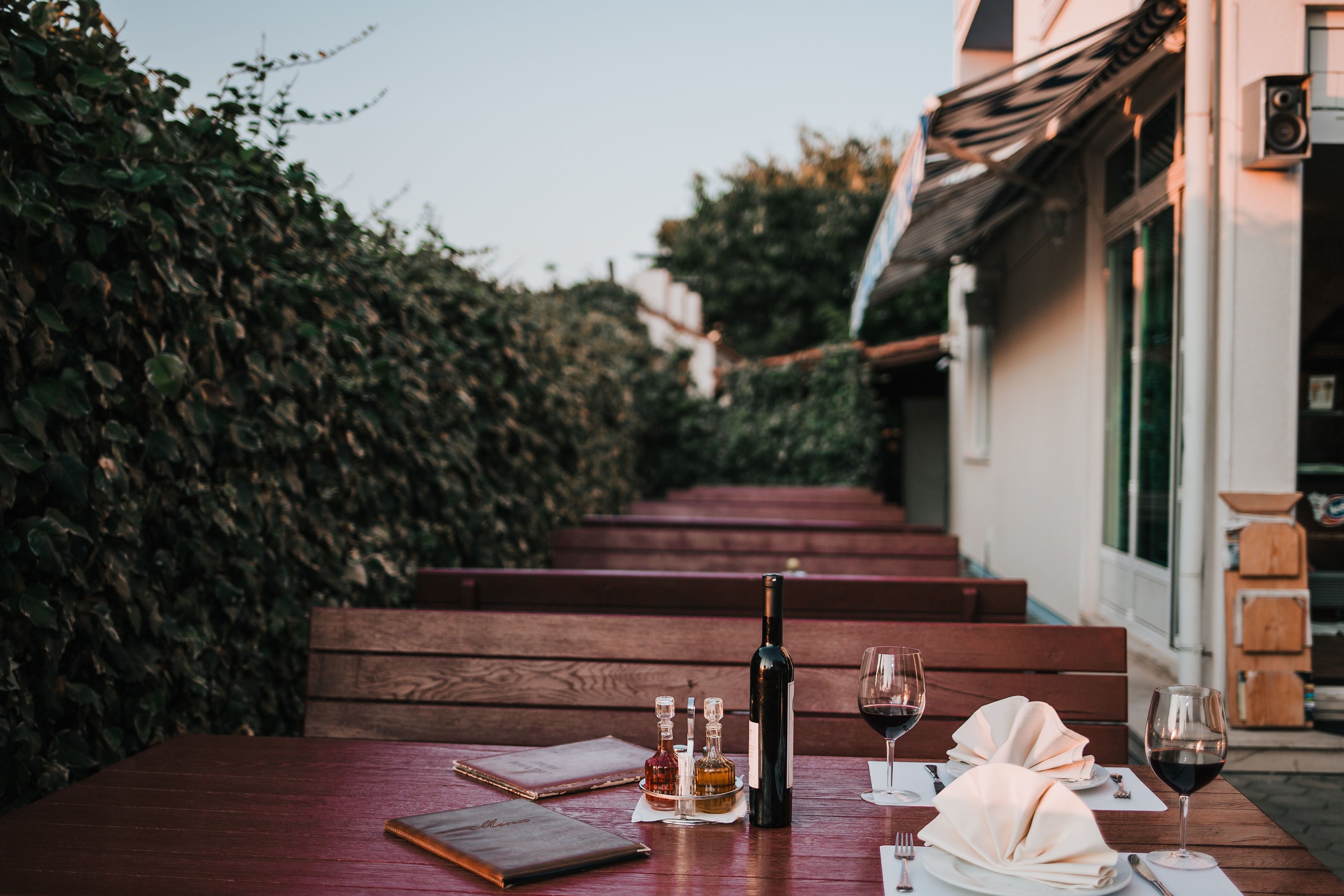 A wooden table set for a meal with a bottle of wine, glasses, and a menu.