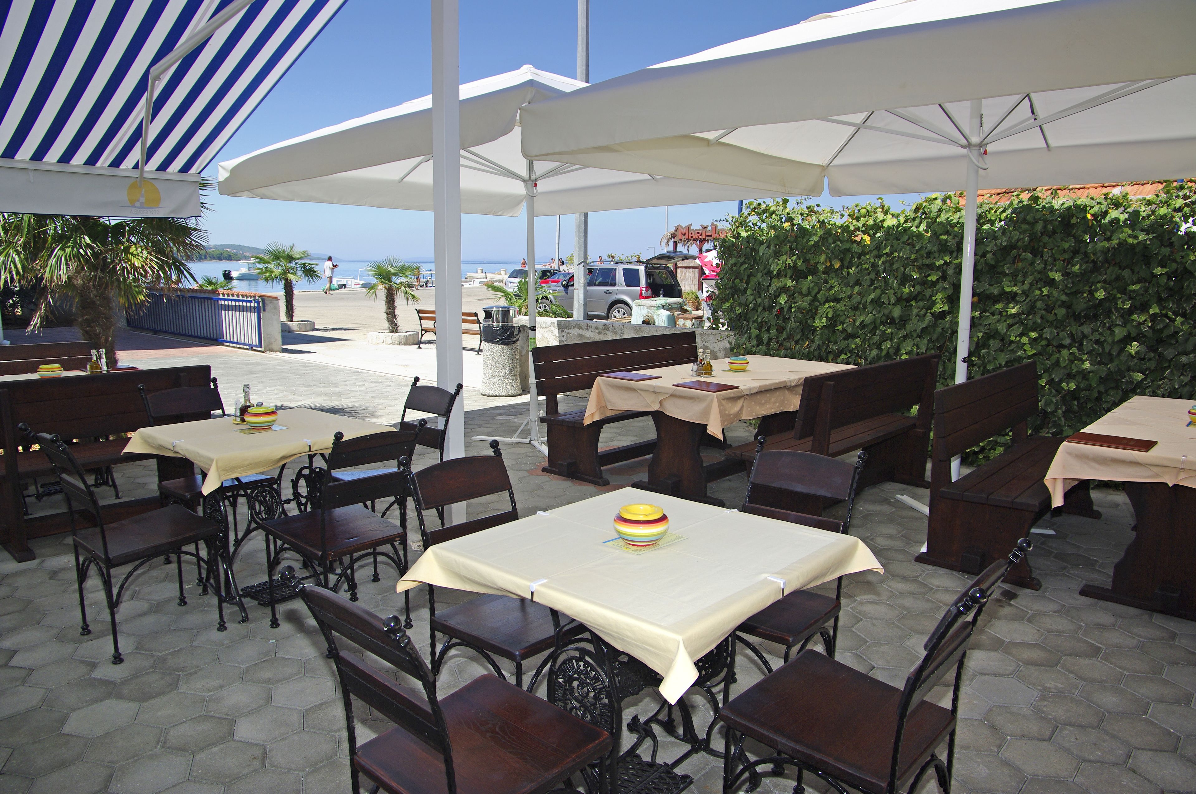 Un espacio de comedor al aire libre con mesas y sillas, sombrillas y vista al mar.