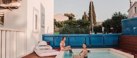 Zona de piscina con suelo de madera, valla azul y edificio con un letrero que dice "MARINA GROMELI RECEPTION".