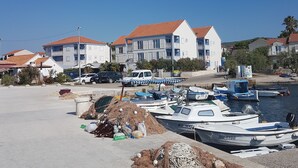 A marina with several boats docked, a pile of fishing nets, and buildings with red-tiled roofs in the background. - Aparthotel Marina Gromela (Supetar)