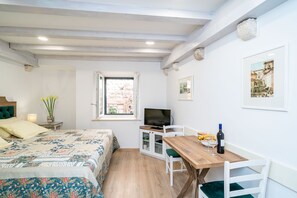 Een slaapkamer met een bed, bureau, televisie en raam.
