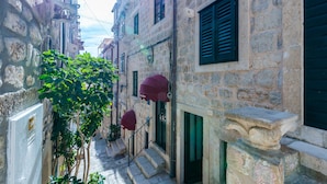 Una calle estrecha con edificios de piedra, una pequeña escalera y un árbol con hojas verdes.
