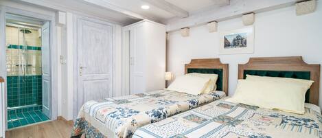 Un dormitorio con cabecera de madera, cama con ropa de cama floral, suelo de madera y baño con zona de ducha de azulejos verdes.
