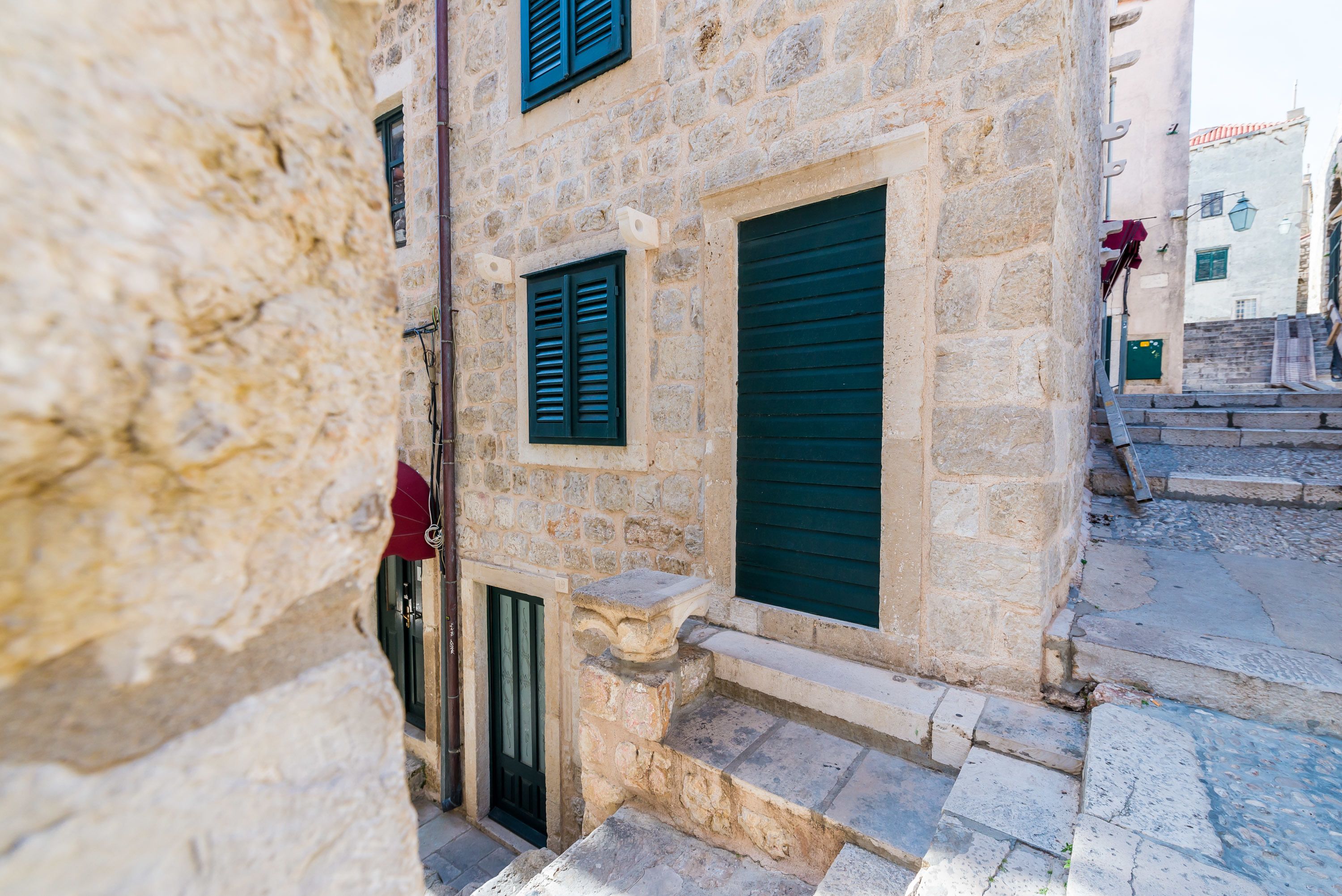 Un edificio de piedra con una entrada estrecha, unos pocos escalones y una puerta con un persiano verde.