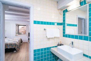 Un dormitorio con cama, ventana y baño con lavamanos y espejo.