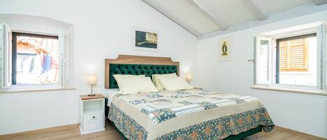 Un dormitorio con una cama de madera, una mesita de noche, un ventanal con contraventanas y un cuadro en la pared.