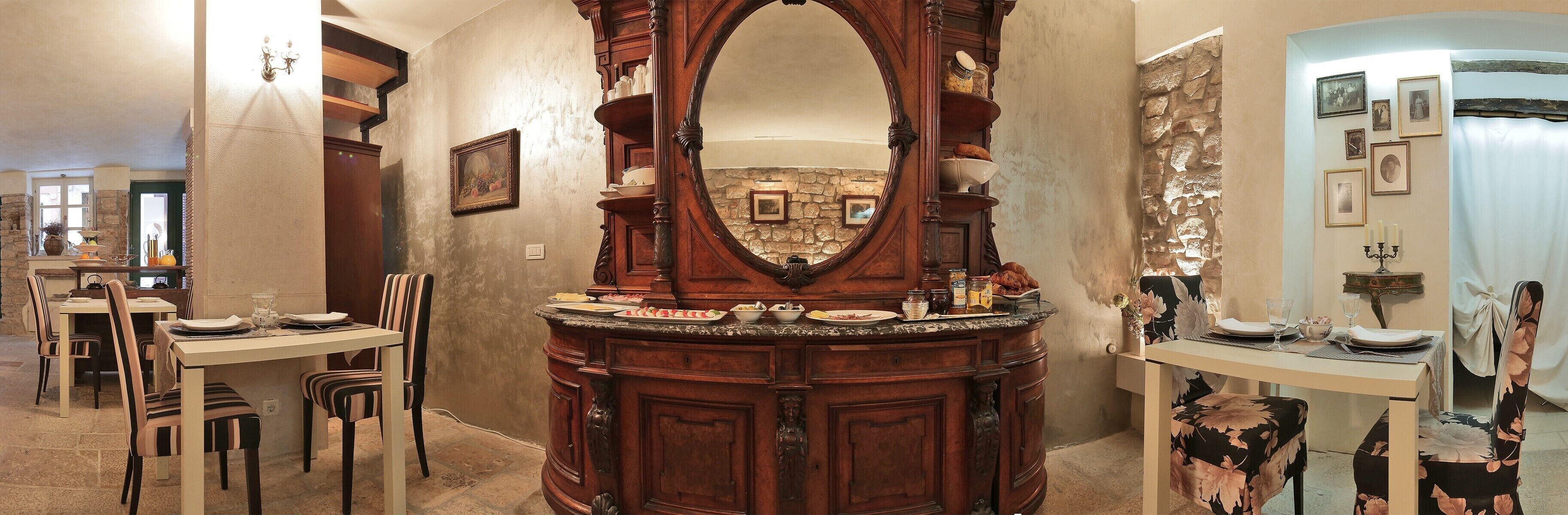 Un comedor con mesa y sillas de madera, un espejo grande y una pared de piedra al fondo.
