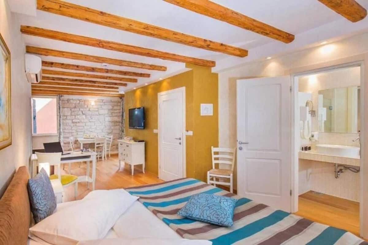 A bedroom with a bed, a desk, a chair, and a bathroom with a mirror and sink.