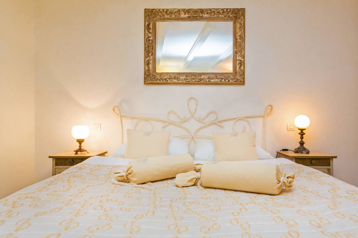 A neatly made bed with a patterned bedspread, two bedside lamps, and a mirror above the headboard.