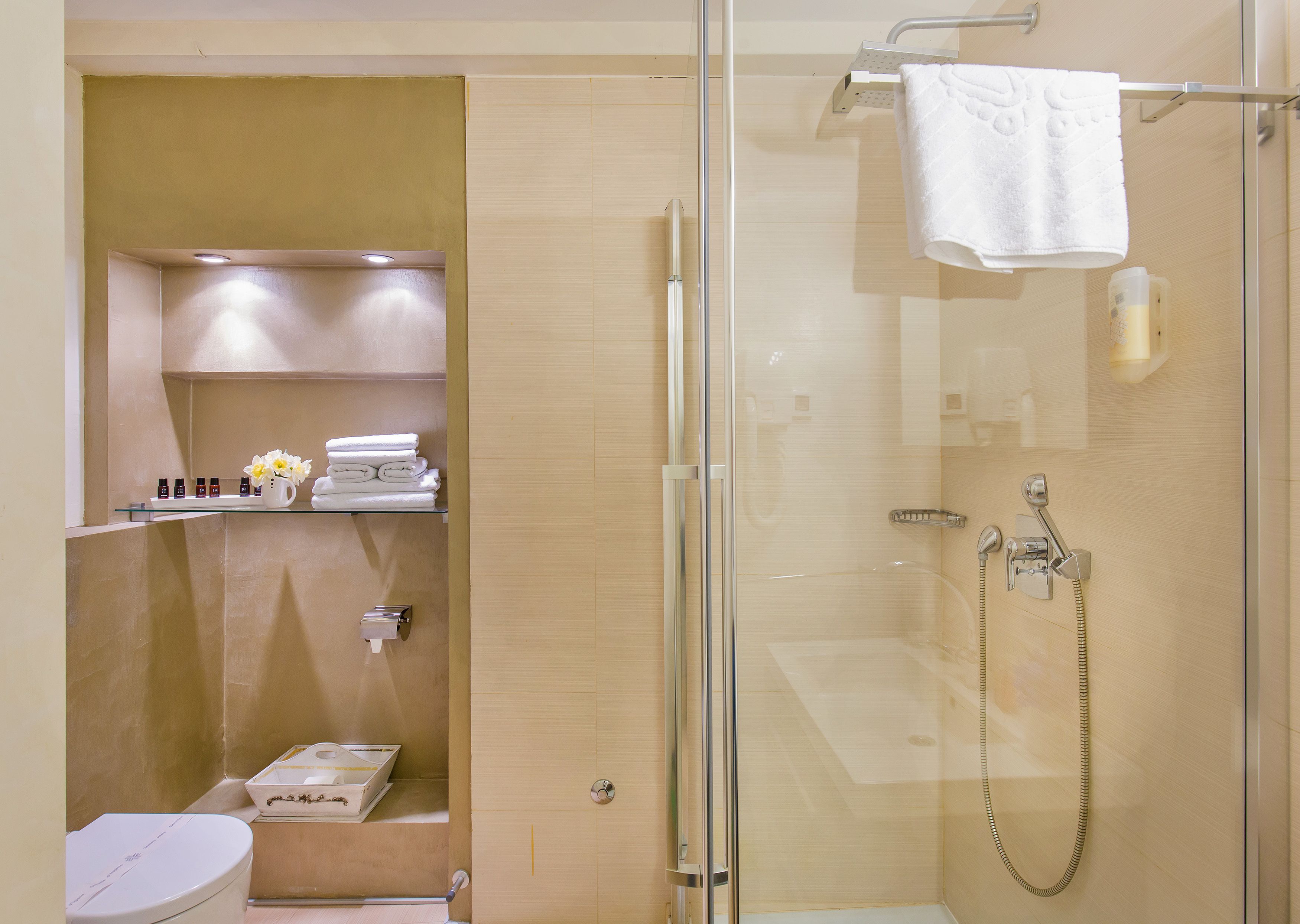 Un baño moderno con ducha de vidrio, inodoro y estante con artículos de aseo.