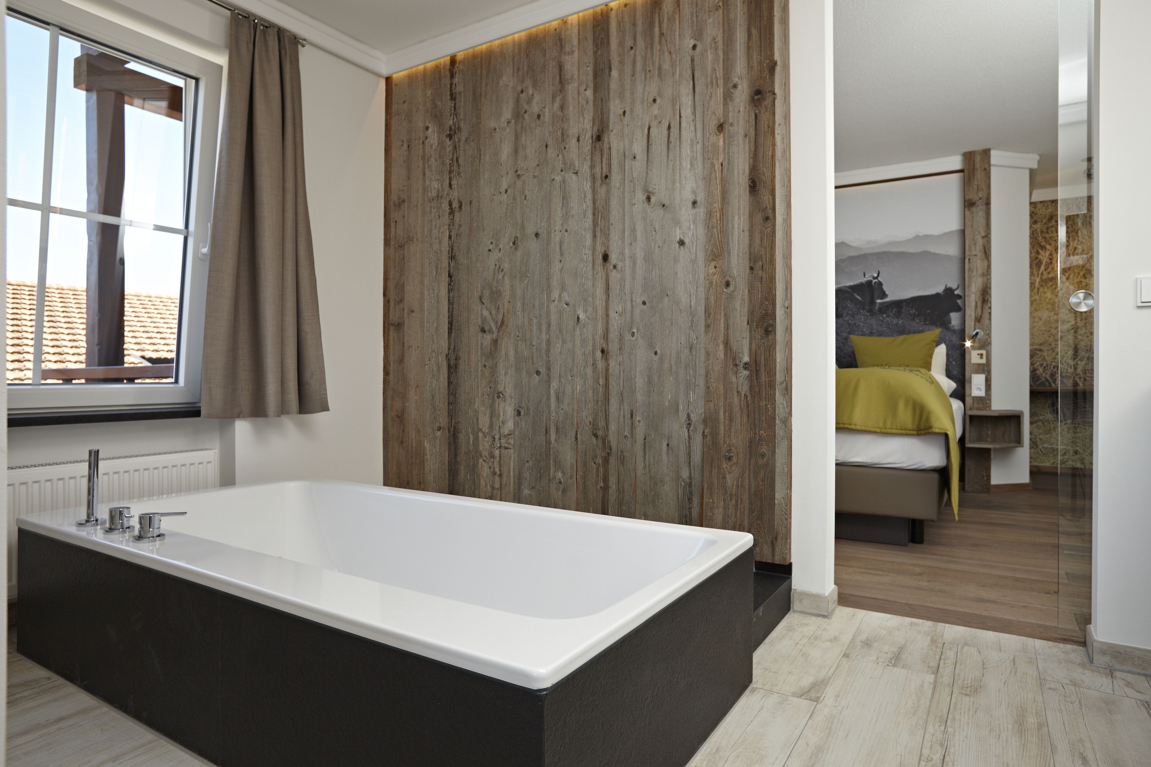Un baño moderno con una bañera grande, un revestimiento de madera y vistas a un dormitorio con cama y un cuadro.