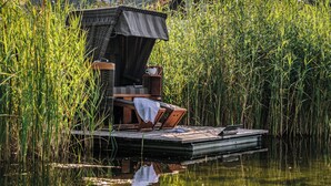 A floating deck with a wicker chair, a small table, and a cup, surrounded by tall reeds. - Haubers Naturresort (Oberstaufen)