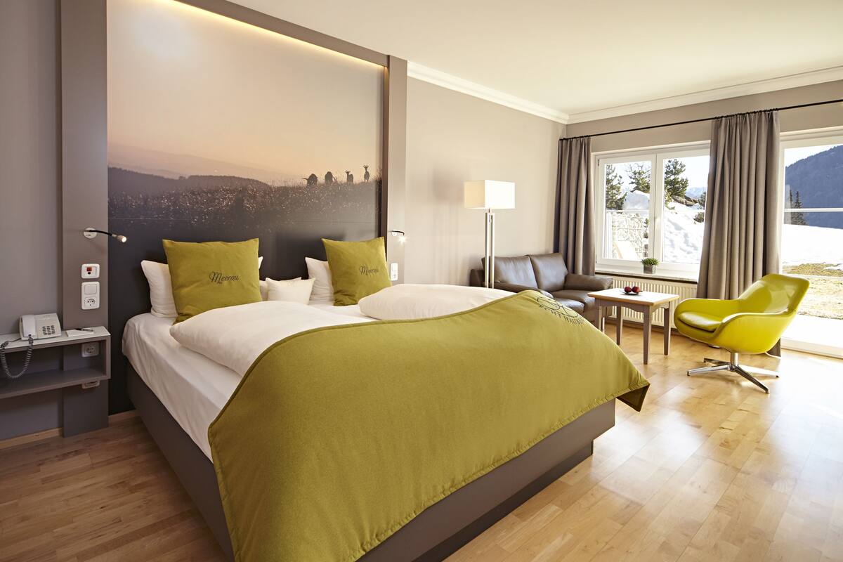 Une chambre d’hôtel avec un grand lit, un bureau, une chaise, une lampe et une vue sur un paysage enneigé.