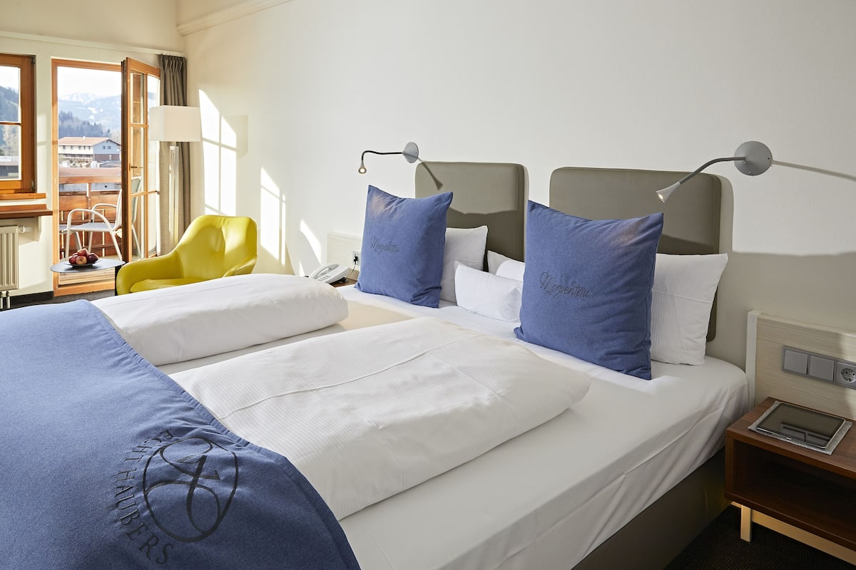 Une chambre d’hôtel avec un grand lit, une chaise, une table de chevet et une fenêtre donnant sur les montagnes.