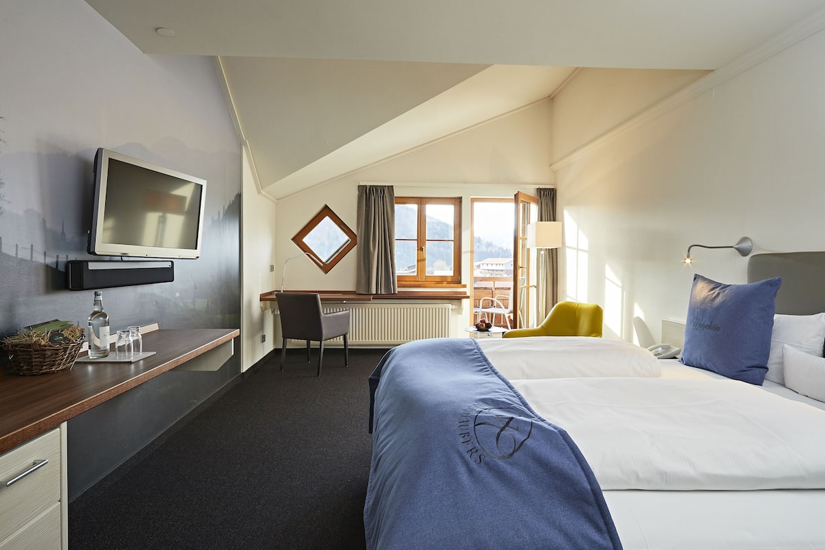 Une chambre d’hôtel équipée d’un lit, d’un bureau, d’une chaise, d’une télévision et d’une fenêtre avec des rideaux.