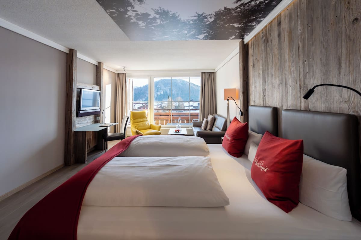 Une chambre d’hôtel avec un lit, un bureau, une chaise, une télévision et une vue sur les montagnes.