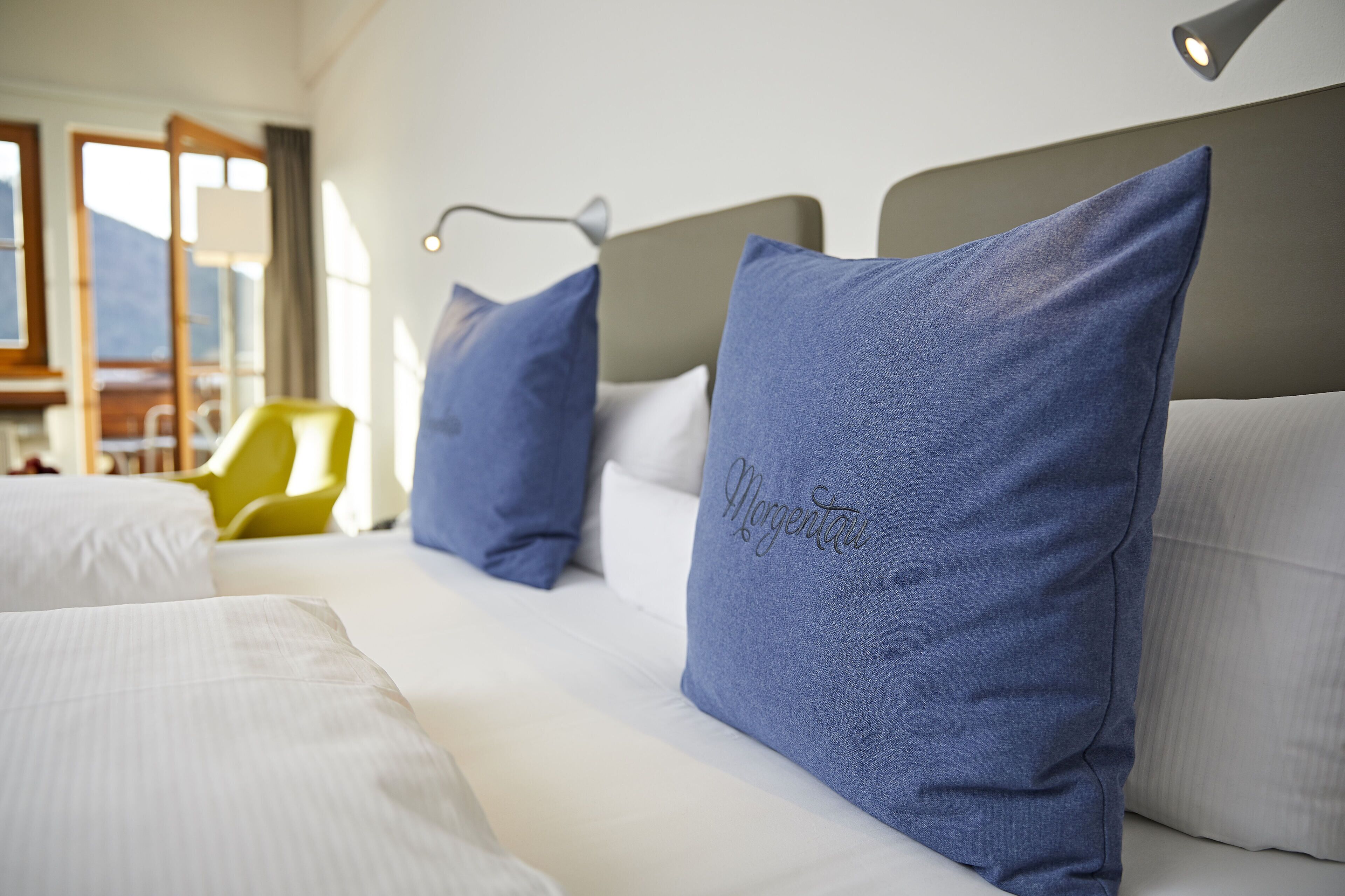 A hotel room with a bed, pillows, a nightstand, and a chair.