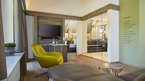 A modern living room with a flat-screen TV, a yellow chair, a gray sofa, and a wooden coffee table. - Haubers Naturresort (Oberstaufen)