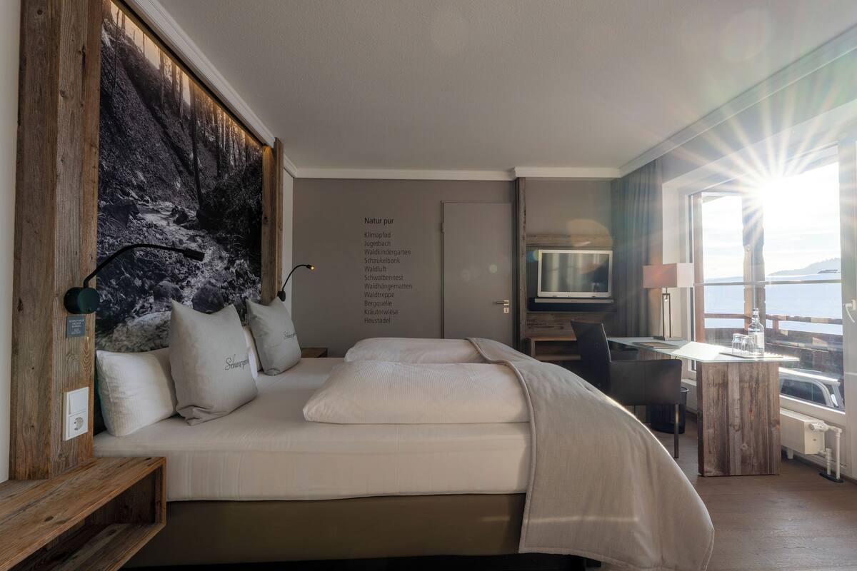 Une chambre d’hôtel moderne dotée d’un grand lit, d’une tête de lit en bois, d’une télévision, d’un bureau et offrant une vue sur la mer.