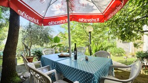 Un área de comedor al aire libre con una mesa cubierta con un mantel azul con lunares blancos, rodeada de sillas de plástico blancas.