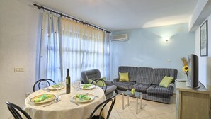 Un área de comedor con una mesa lista para dos personas, un sofá y un televisor sobre un mueble.