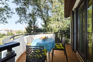 A balcony with a table and chairs, a view of trees, and a building in the background.