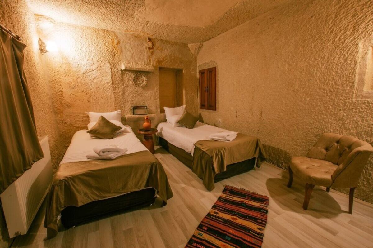 A room with two beds, a chair, a small table, and a wall-mounted shelf.