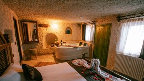 A room with a large bed, a bathtub, and a wooden door. - Mia Cappadocia Cave Hotel (Nevsehir)