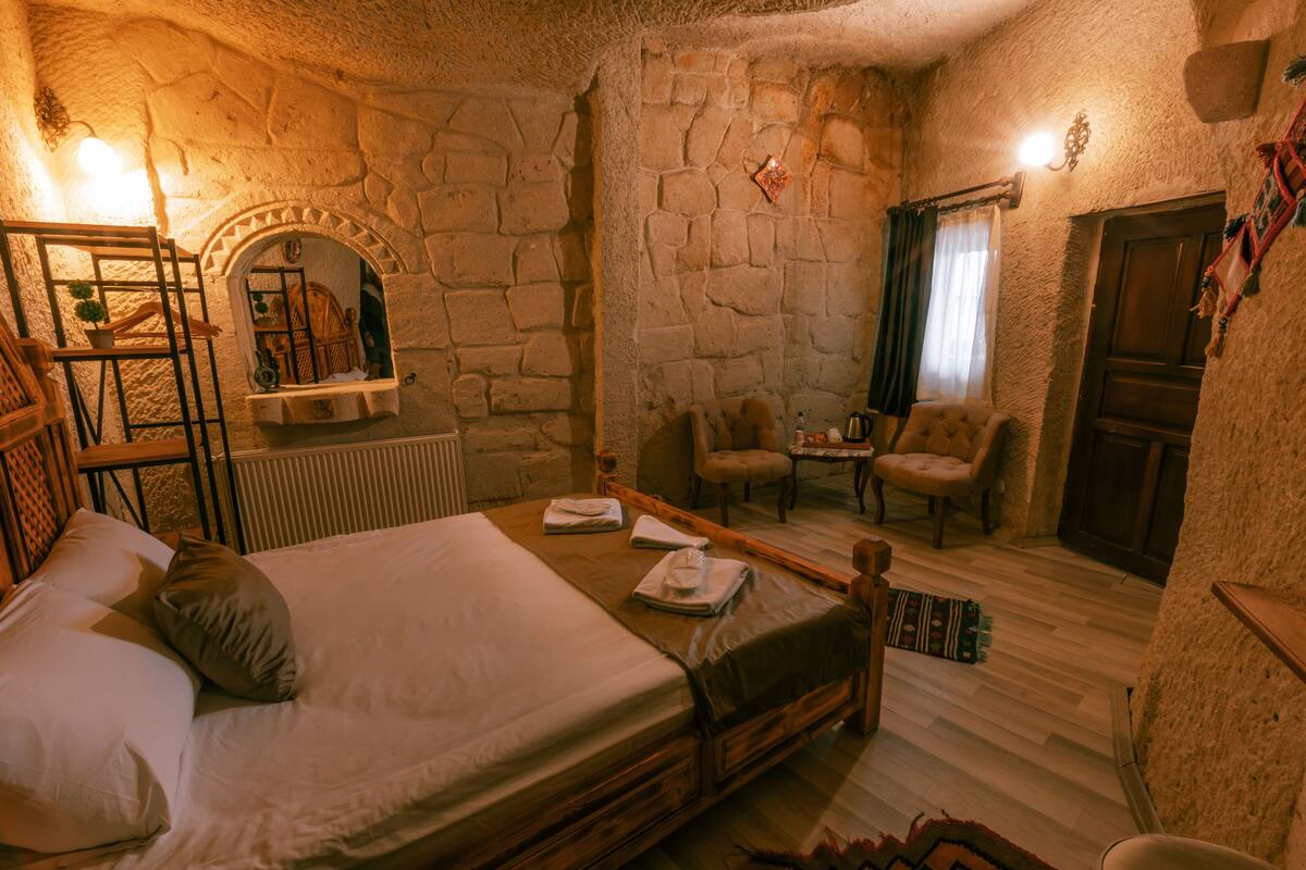 A cozy room with a bed, two chairs, a small table, and a stone wall.