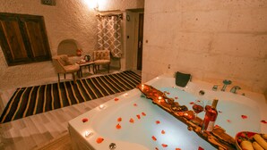 A spa room with a large bathtub, a wooden bench, and a small table with a bottle and glasses. - Mia Cappadocia Cave Hotel (Nevsehir)