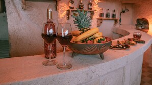 A bar area with a rustic stone wall, a bottle of wine, two glasses, a bowl of fruit, and various bottles on shelves. - Mia Cappadocia Cave Hotel (Nevsehir)
