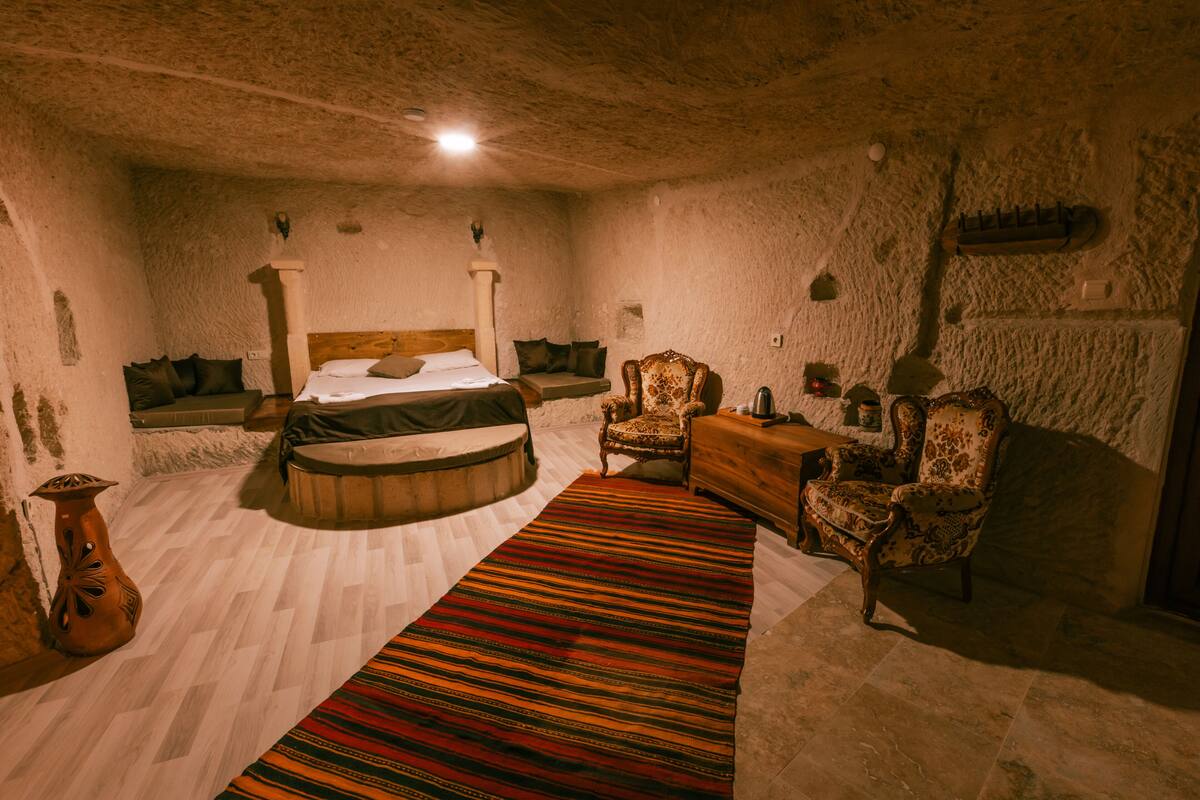 A room with a bed, two chairs, a small table, and a decorative rug.