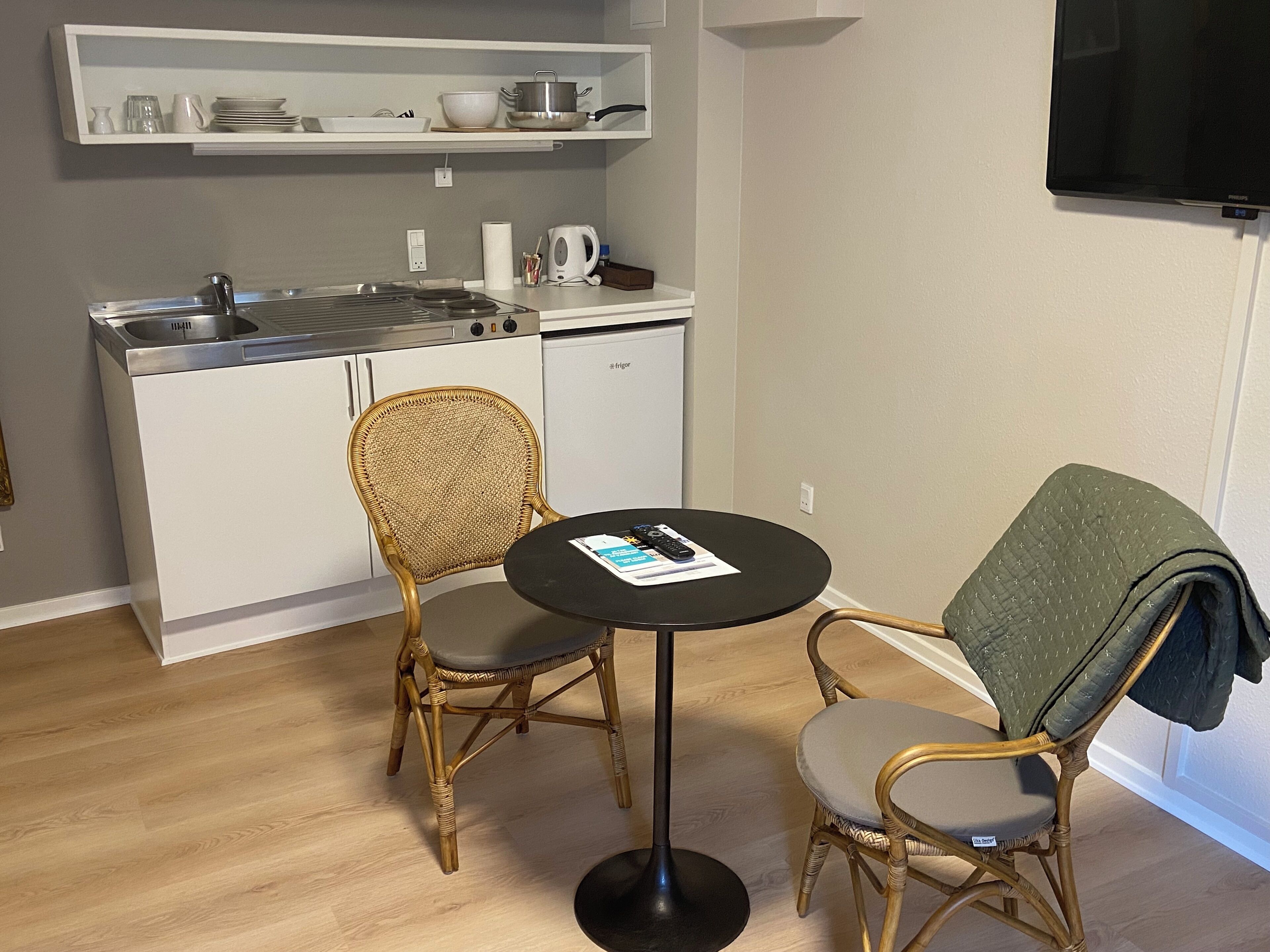 A compact kitchenette with white cabinets, a built-in stove, and a small dining area with two wicker chairs and a round table.