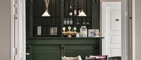 Zona de bar con paneles de madera oscura, iluminación colgante y estantes con botellas y vasos.