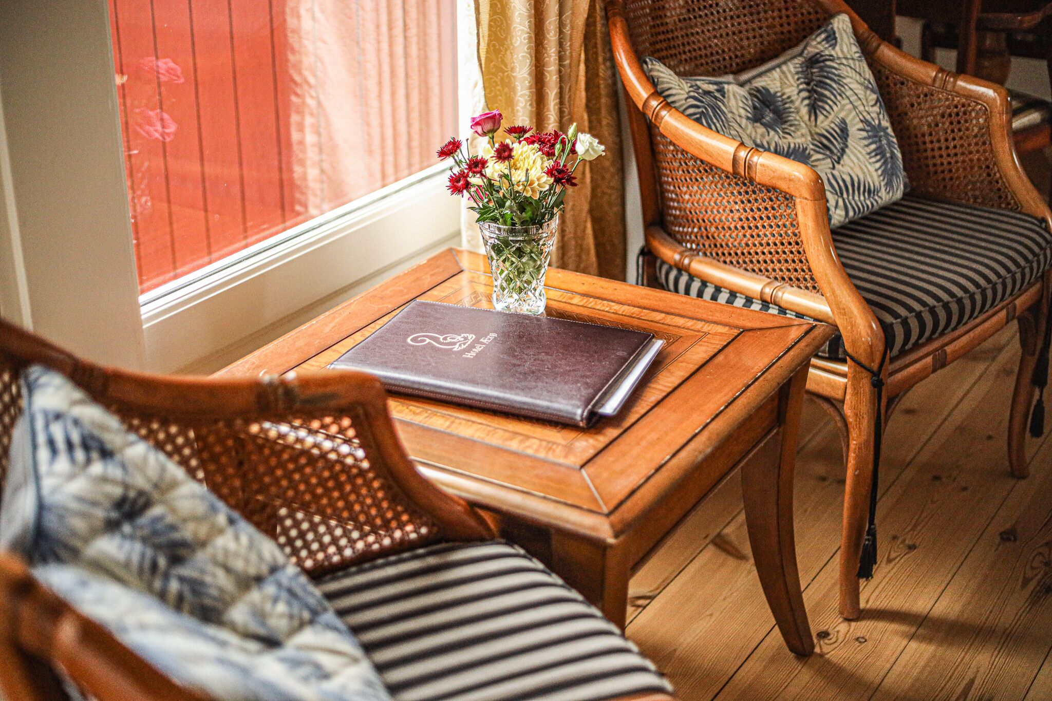 A wooden table with a laptop and a vase of flowers. There are wicker chairs with striped cushions.