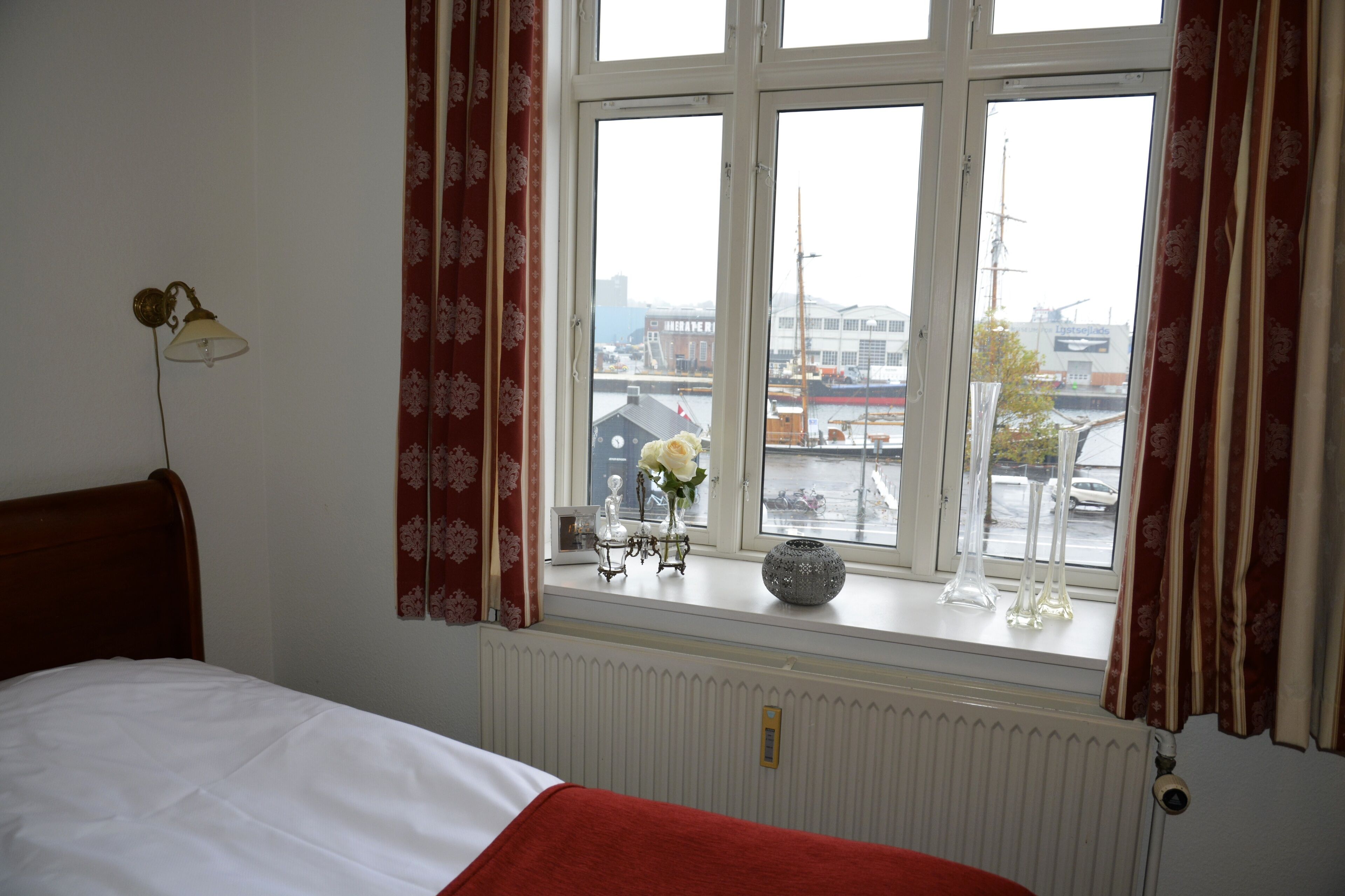 Une chambre à coucher avec un lit, une fenêtre avec des rideaux, un radiateur et une vue sur la ville.