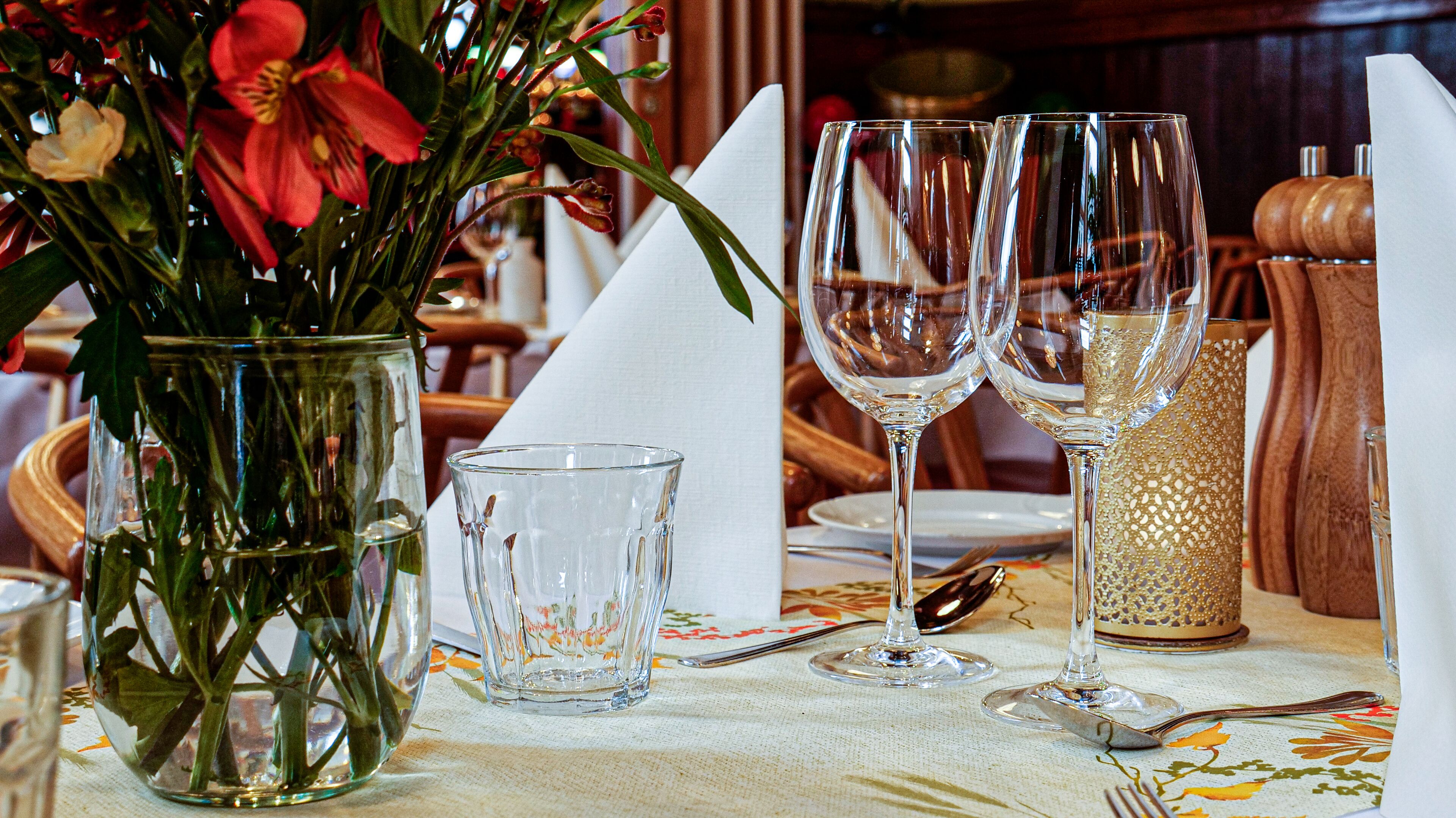 A table set for dining with a vase of flowers, clear glasses, and a candle holder.