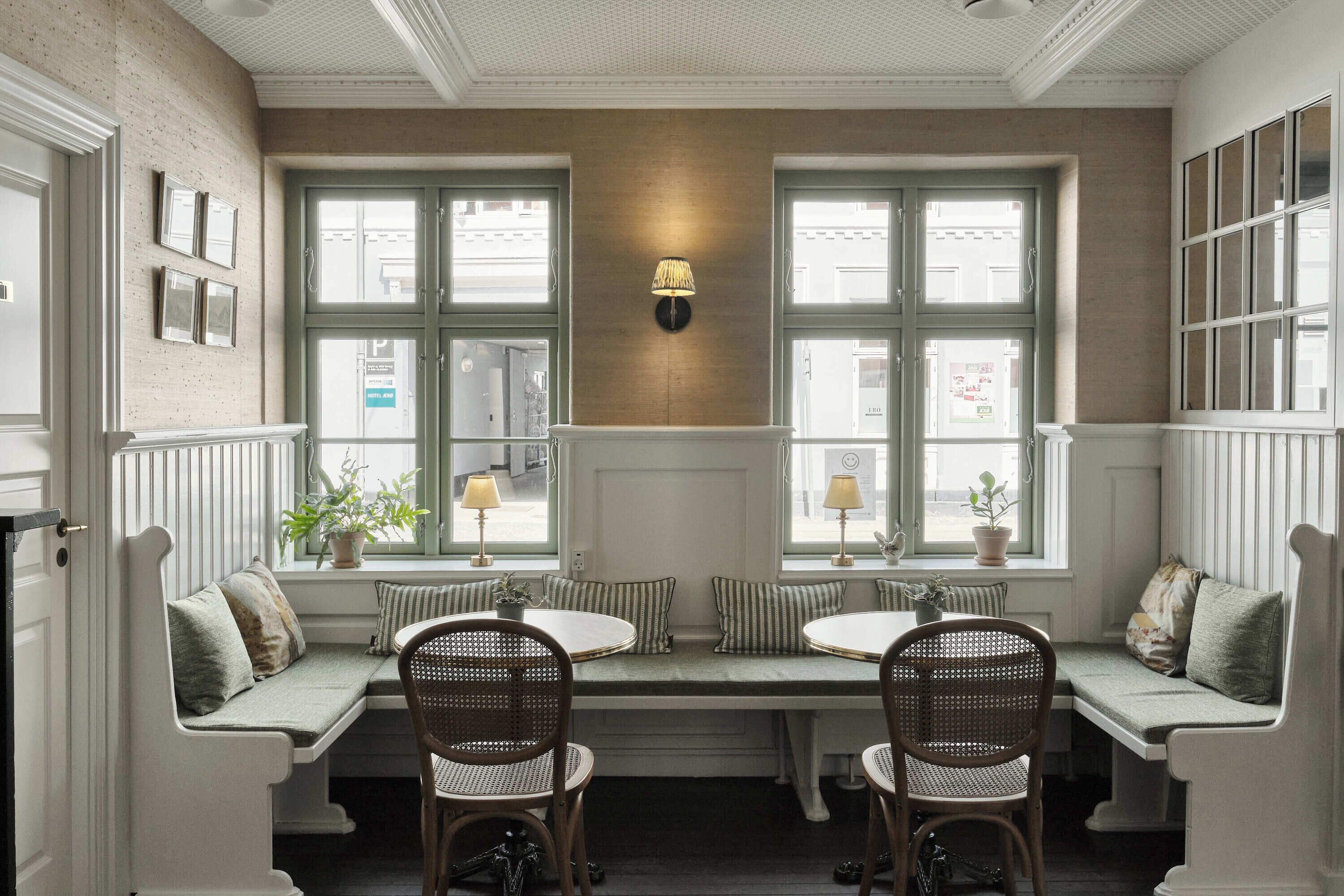 A cozy seating area with a bench and two chairs, a wall-mounted lamp, and a window with a view of the street.