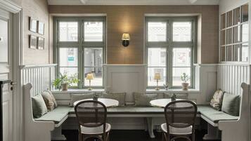 A cozy seating area with a bench and two chairs, a wall-mounted lamp, and a window with a view of the street.