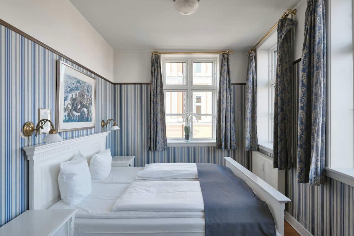 A hotel room with a large bed, a bedside table, a window with curtains, and a framed picture on the wall.