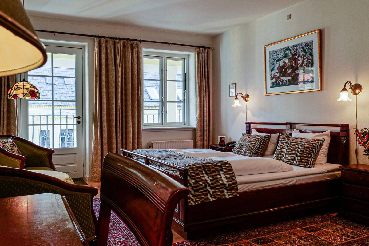 A hotel room with a large bed, a chair, a table, and a window with curtains.
