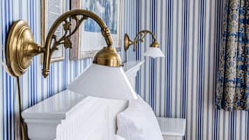 Un baño con un lavamanos blanco, un grifo dorado y una lámpara blanca fijada a la pared.