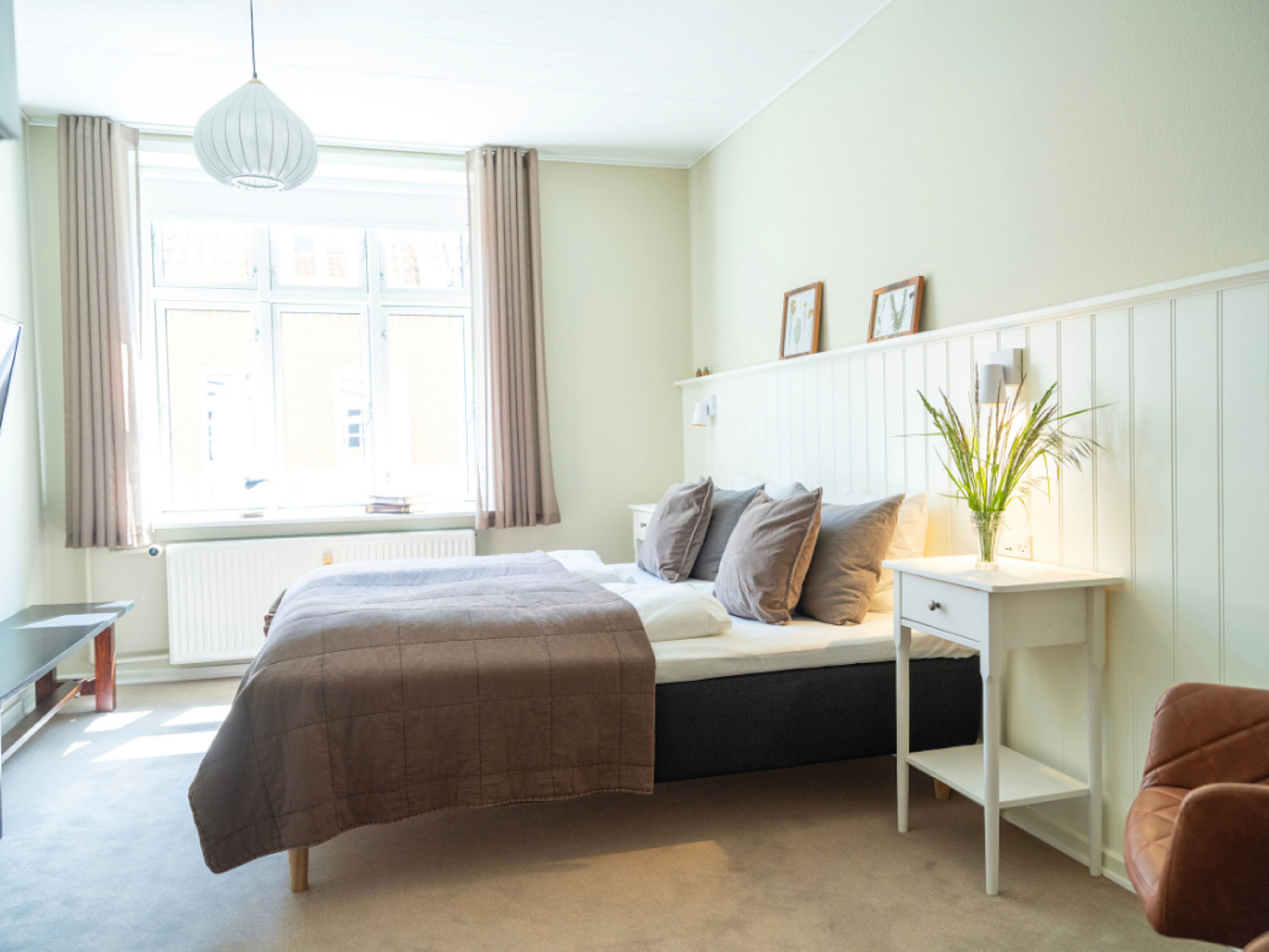 Ein Schlafzimmer mit Bett, Nachttisch, Lampe und einem Fenster mit Vorhängen.