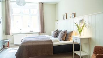Ein Schlafzimmer mit Bett, Nachttisch, Lampe und einem Fenster mit Vorhängen.