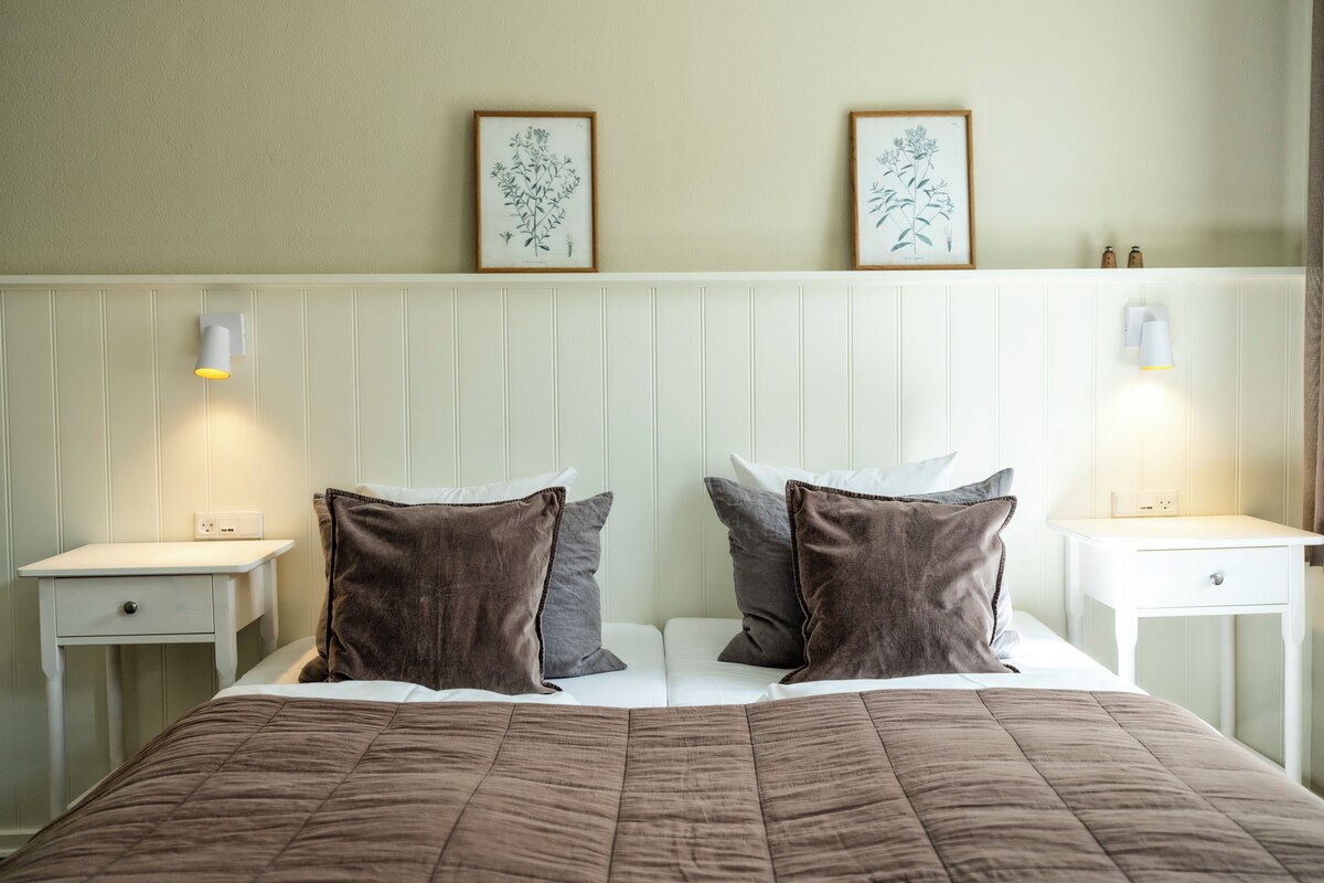 A neatly made bed with a brown quilt, two pillows, and a headboard with wall-mounted lamps.