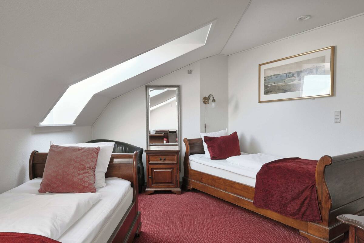 A bedroom with two beds, a wooden dresser, a mirror, and a skylight.