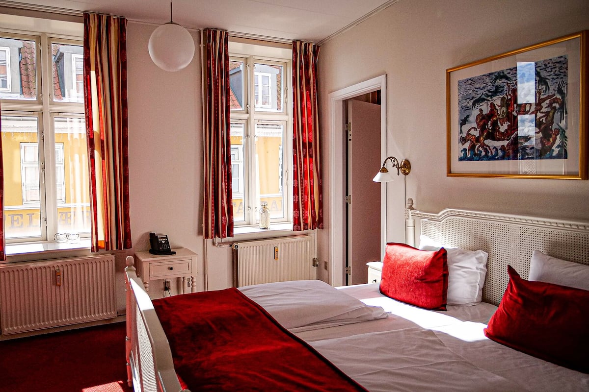A hotel room with a bed, a radiator, a telephone, and a painting on the wall.