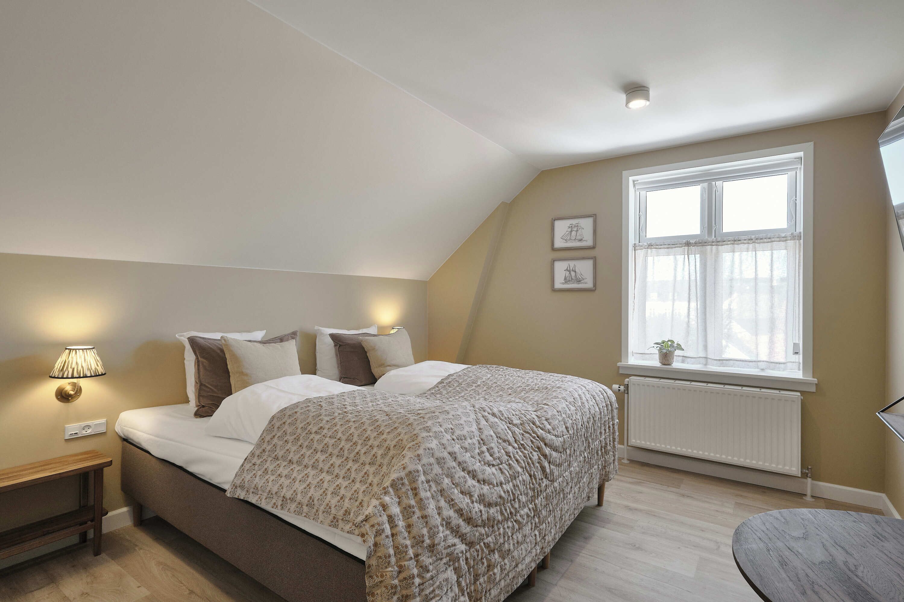 A bedroom with a bed, bedside lamps, a window with curtains, and a radiator.